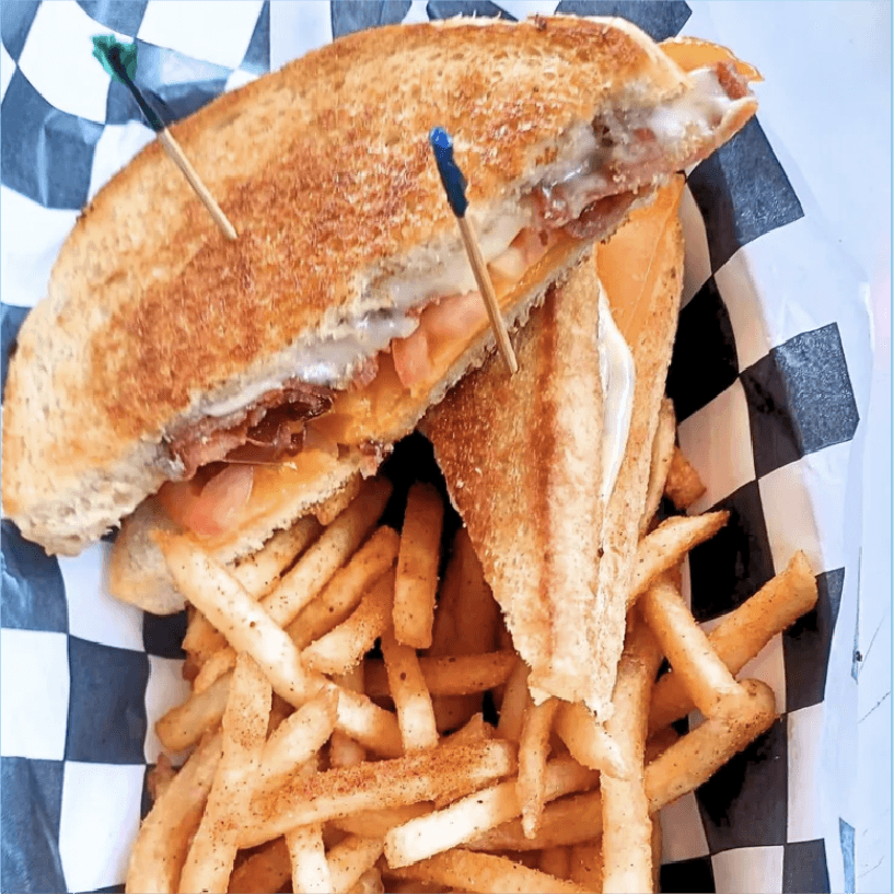 A grilled cheese sandwich with bacon and seasoned fries in a checkered basket